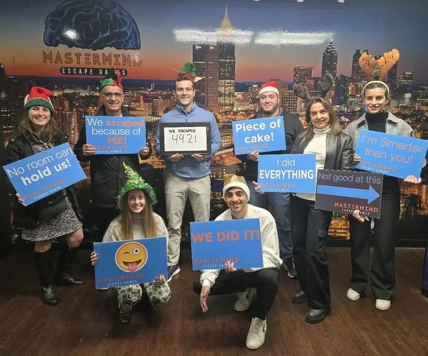 A team in holiday hats and antlers holding Mastermind signs, including one with an escape time of 49:21