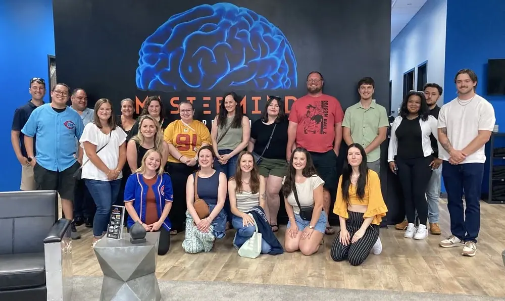 A large group posing together under the Mastermind brain mural